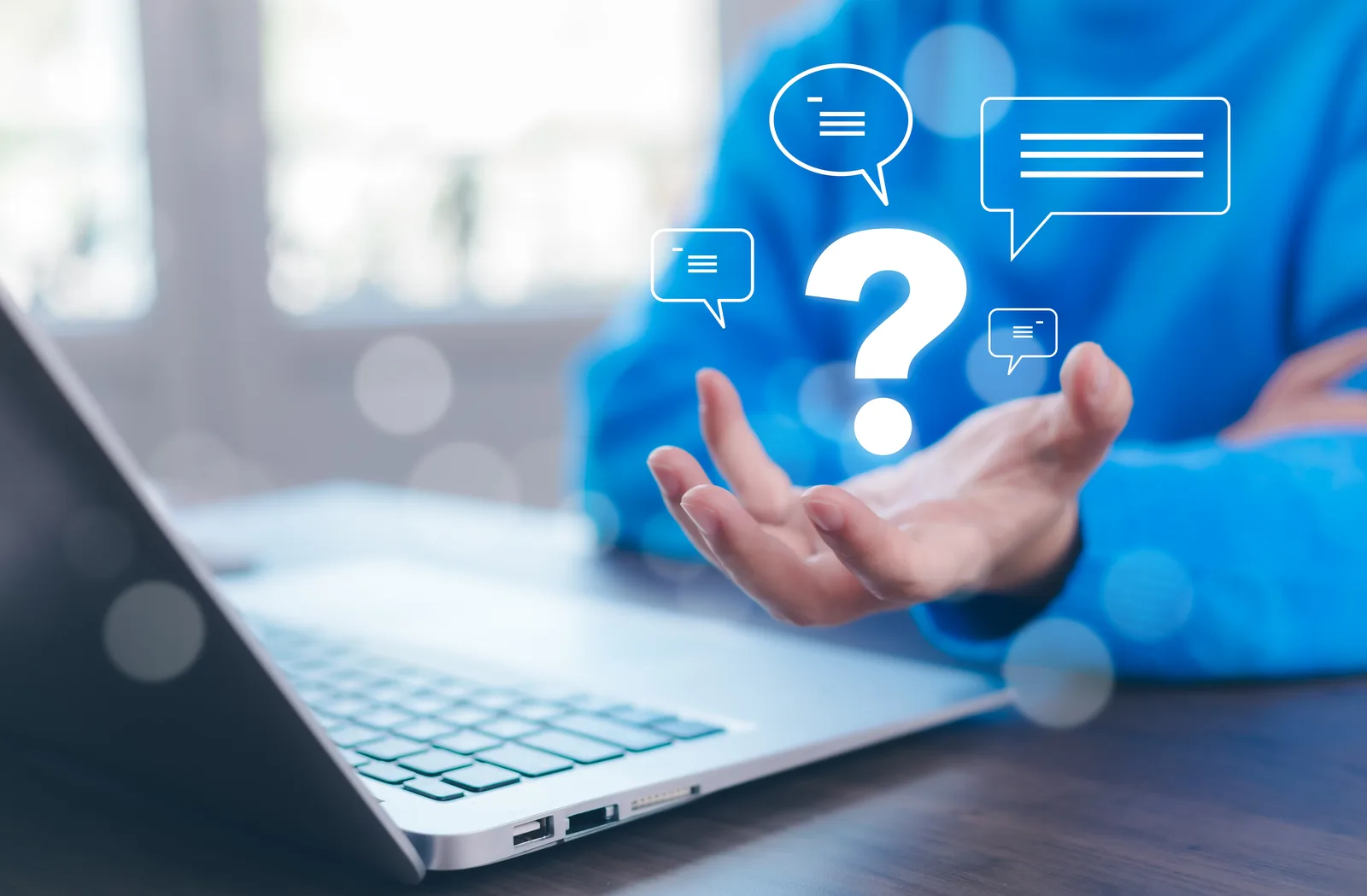 Person at a laptop with an open hand underneath a question mark surrounded by speech-bubble icons, representing the questions, situations, or experiences that are signs it may be time to talk to a lawyer.
